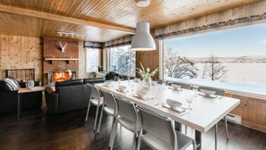 Un interior moderno con chimenea, zona de comedor y ventanas amplias con vistas a un paisaje nevado.