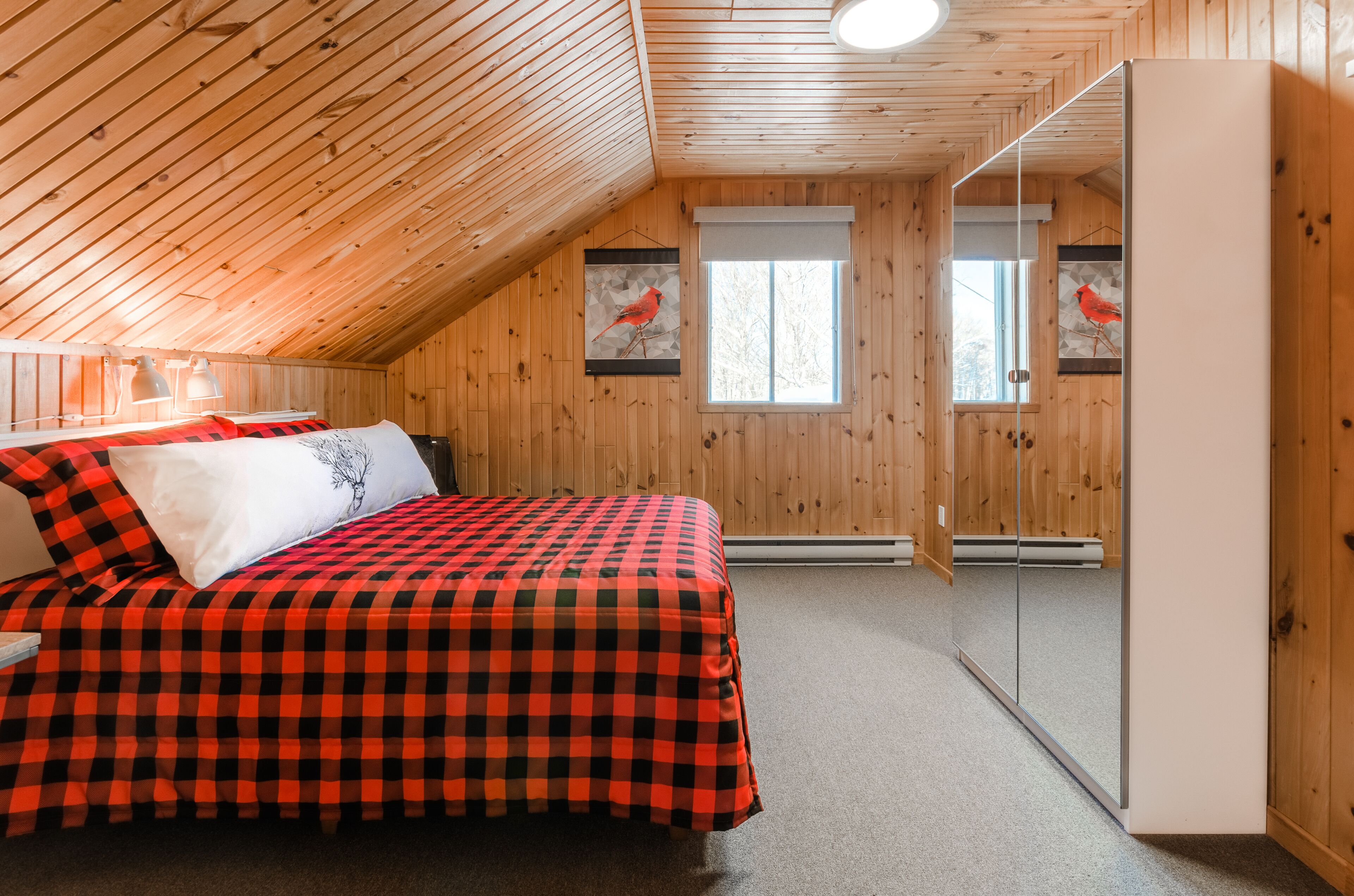A bedroom with a checkered bedspread, two wall-mounted lamps, and a large mirror.