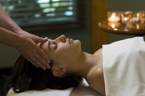Une personne reçoit un massage de la tête dans une pièce où une table éclairée à la bougie se trouve à l'arrière-plan.