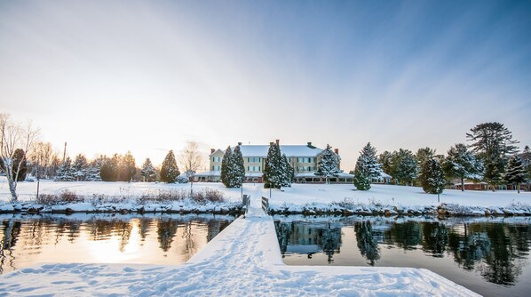 Une grande maison, avec un paysage enneigé et un étang au premier plan.