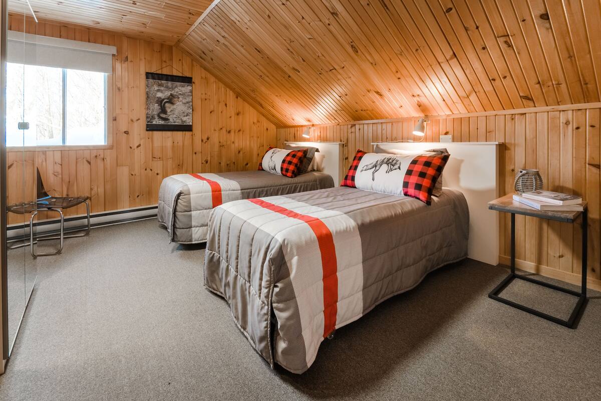 A cozy attic bedroom with two beds, a small table, and a chair.