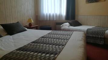 A hotel room with a large bed, two smaller beds, a patterned throw, a lamp, and a painting on the wall.