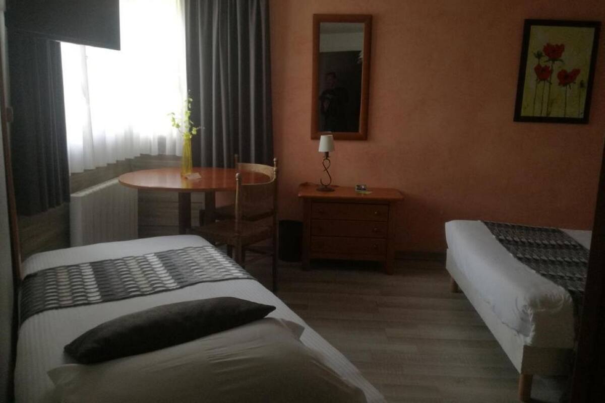 A hotel room with two beds, a small desk, a chair, a lamp, and a painting on the wall.