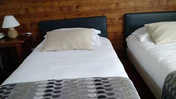 A room with two beds, each with a headboard and pillows. There is a lamp on a side table next to the left bed.