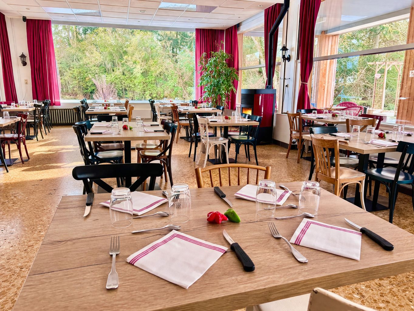 Un restaurant doté de nombreuses tables, de chaises et d’une grande fenêtre offrant une vue sur la verdure.