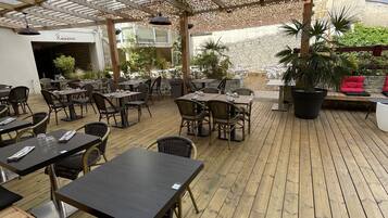 An outdoor patio with wooden tables and chairs, a ceiling fan, and a reception area.