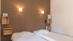 A hotel room with two beds, wooden headboards, and wall-mounted light fixtures. - Hôtel de L'Ecu (Jonzac)
