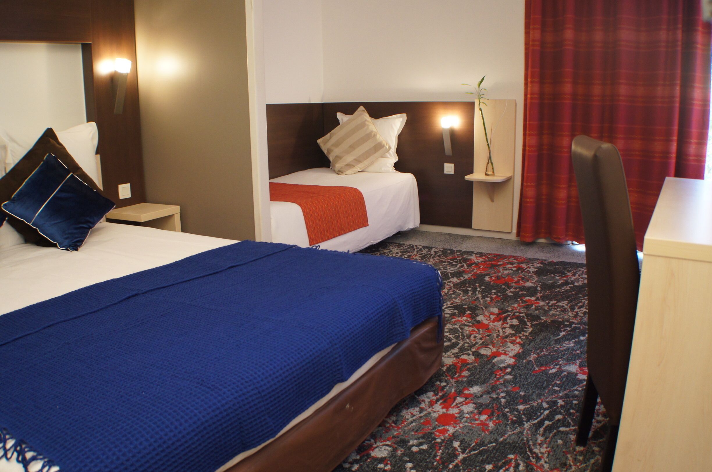 A hotel room with two beds, a desk, a chair, and a red curtain.
