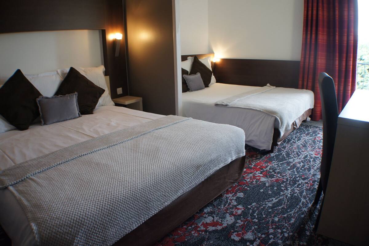 Dos camas con cabeceras, una mesita de noche y una alfombra estampada en una habitación de hotel.