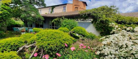 Hotel La Siesta, con un jardín con arbustos verdes y flores rosadas.