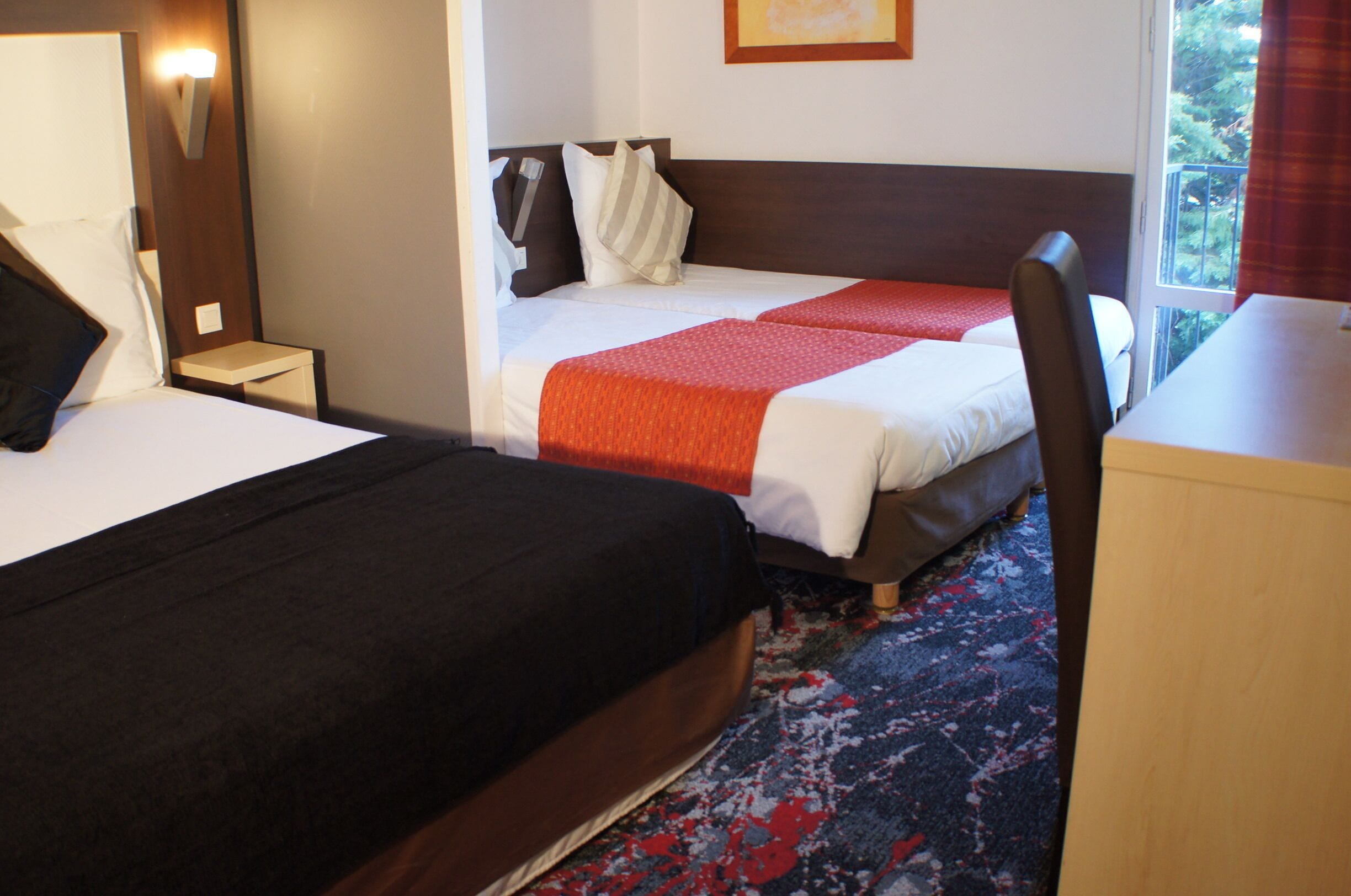 Une chambre d’hôtel avec deux lits, un bureau et une fenêtre donnant sur des arbres.