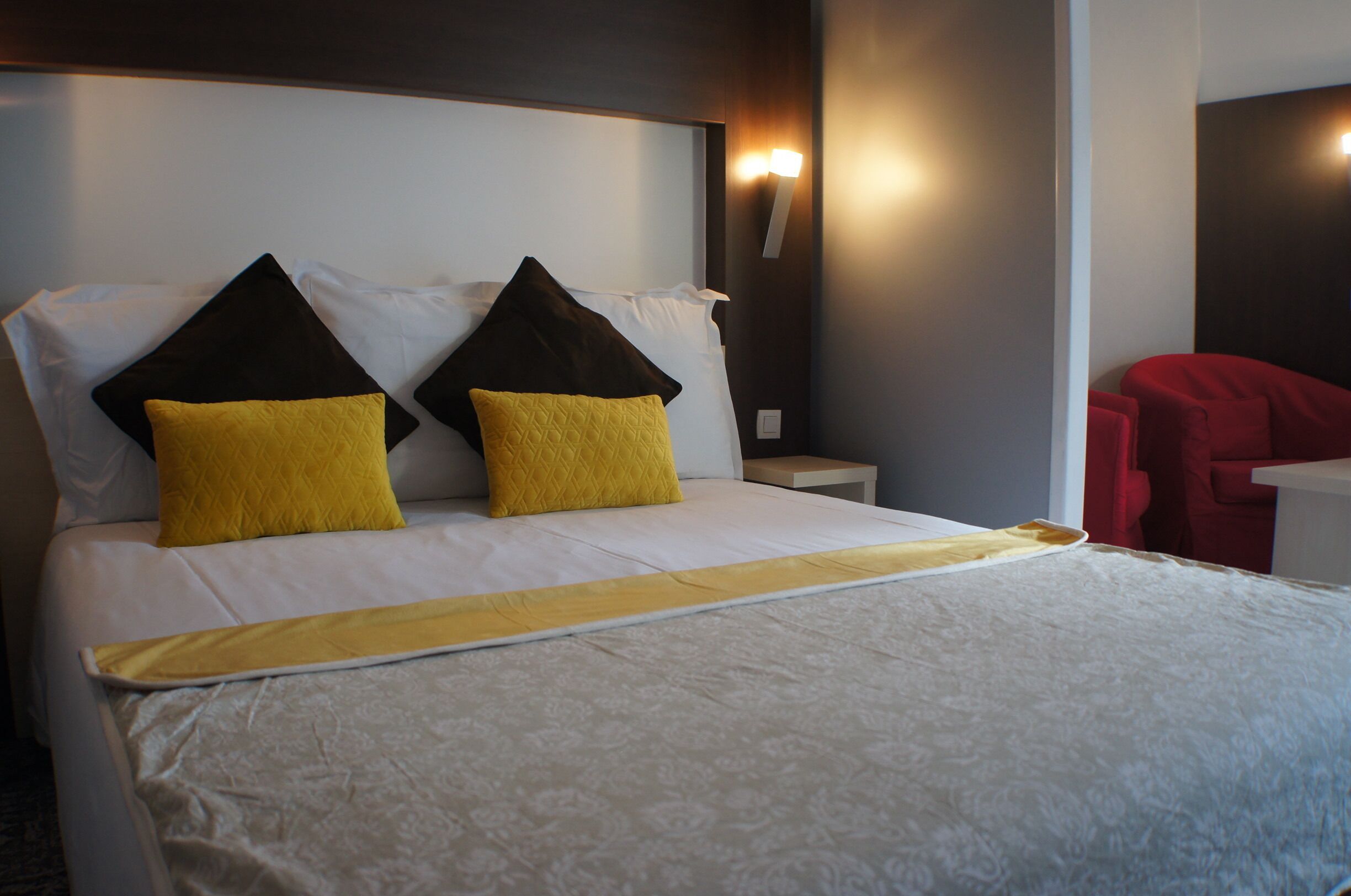A neatly made bed with white and yellow bedding, two black pillows, and a red chair in the corner.