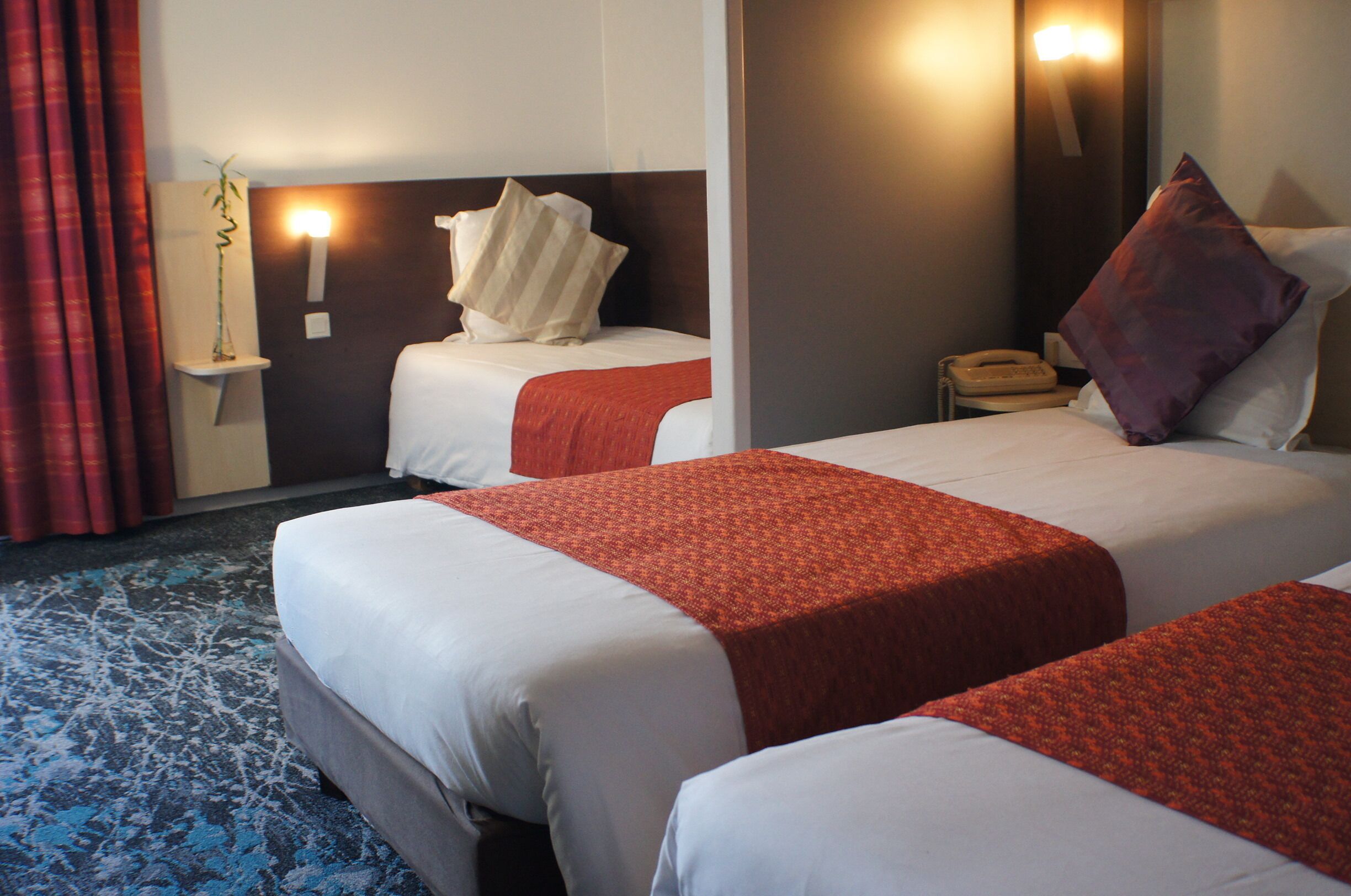 A hotel room with two beds, a bedside table with a telephone, and a wall-mounted light fixture.