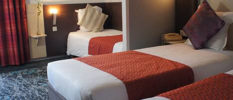 A hotel room with two beds, a bedside table with a telephone, and a wall-mounted light fixture.