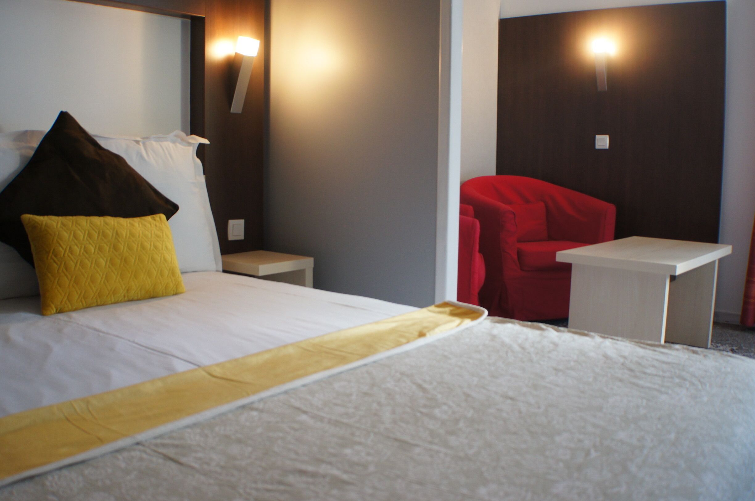 Une chambre d’hôtel avec un lit, une table de chevet, une chaise rouge et une petite table.