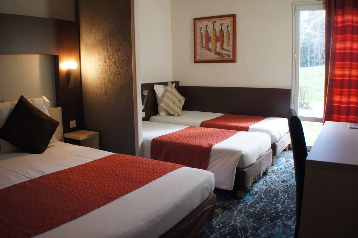 Habitación de hotel con tres camas, un escritorio y una ventana con cortinas.