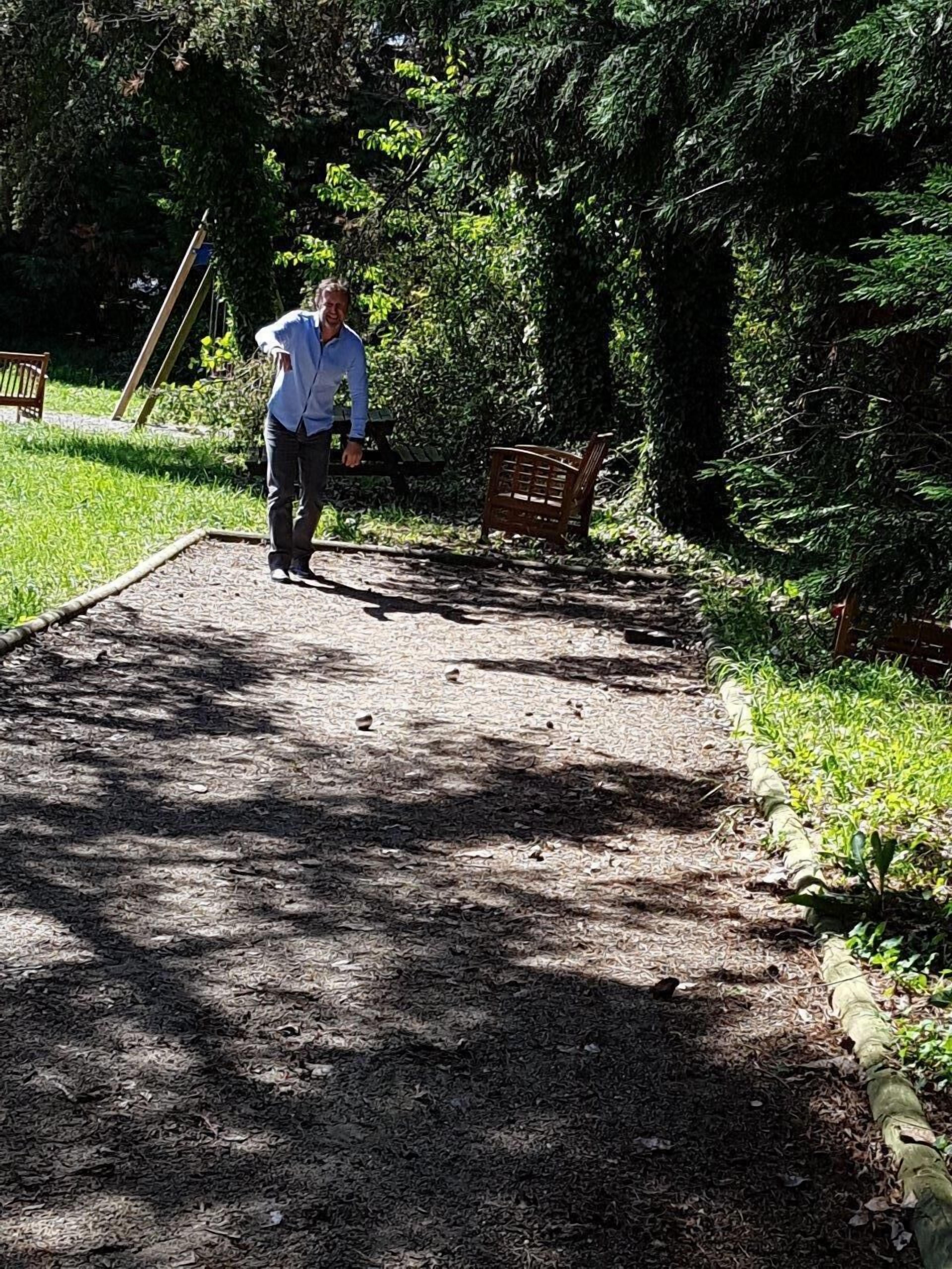 A person walking on a gravel path in a park with benches and dense foliage.