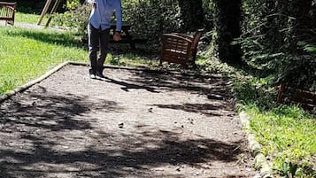 A person walking on a gravel path in a park with benches and dense foliage.