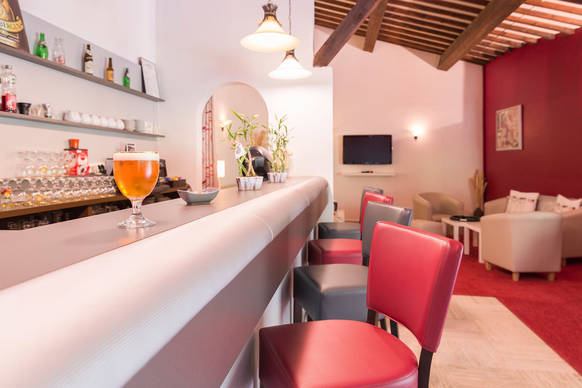 Un coin bar avec un verre de bière, une étagère remplie de bouteilles et un téléviseur en arrière-plan.