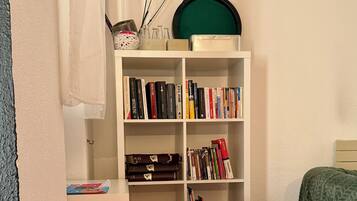 A room with a white bookshelf, a pink chair, a small table with a toy and a book, and a bed with a green blanket.