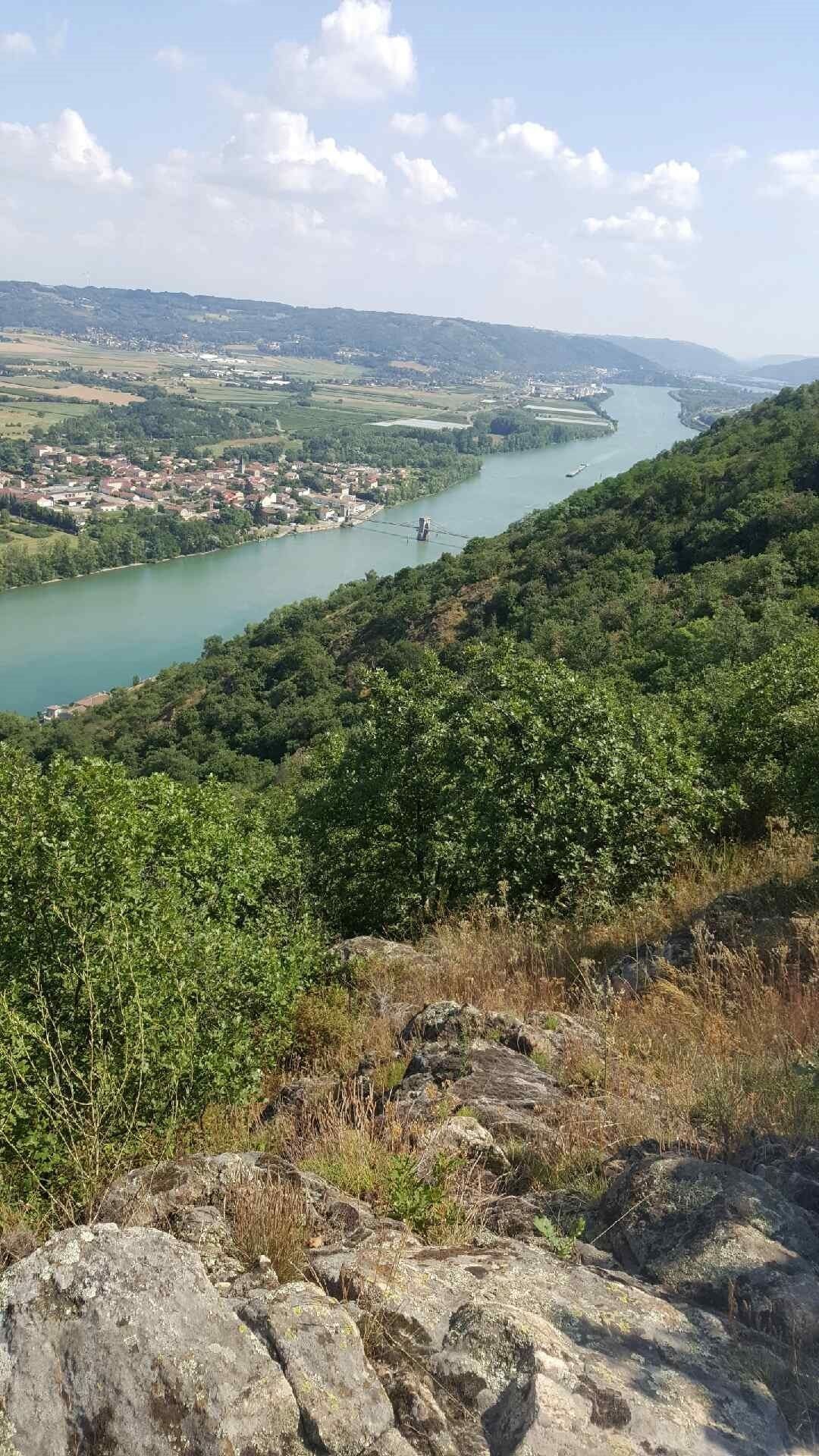 A river with a town on the opposite bank, surrounded by hills and greenery.