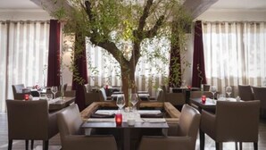 A dining area with tables set for four, surrounded by chairs, and a large tree in the center. - Hôtel Restaurant L'Etape (Bouc-Bel-Air)