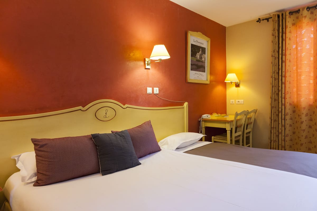 A hotel room with a bed, two wall-mounted lamps, a framed picture, and a small table with chairs.