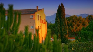 A building with a sign that reads "Hotel de la Plagne" surrounded by greenery and mountains in the background. - Hôtel Restaurant L'Etape (Bouc-Bel-Air)
