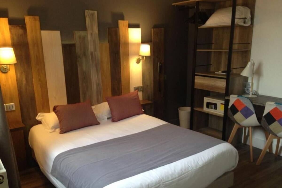 A bedroom with a bed, wooden headboard, bedside lamps, a wardrobe, and a chair with a colorful cushion.