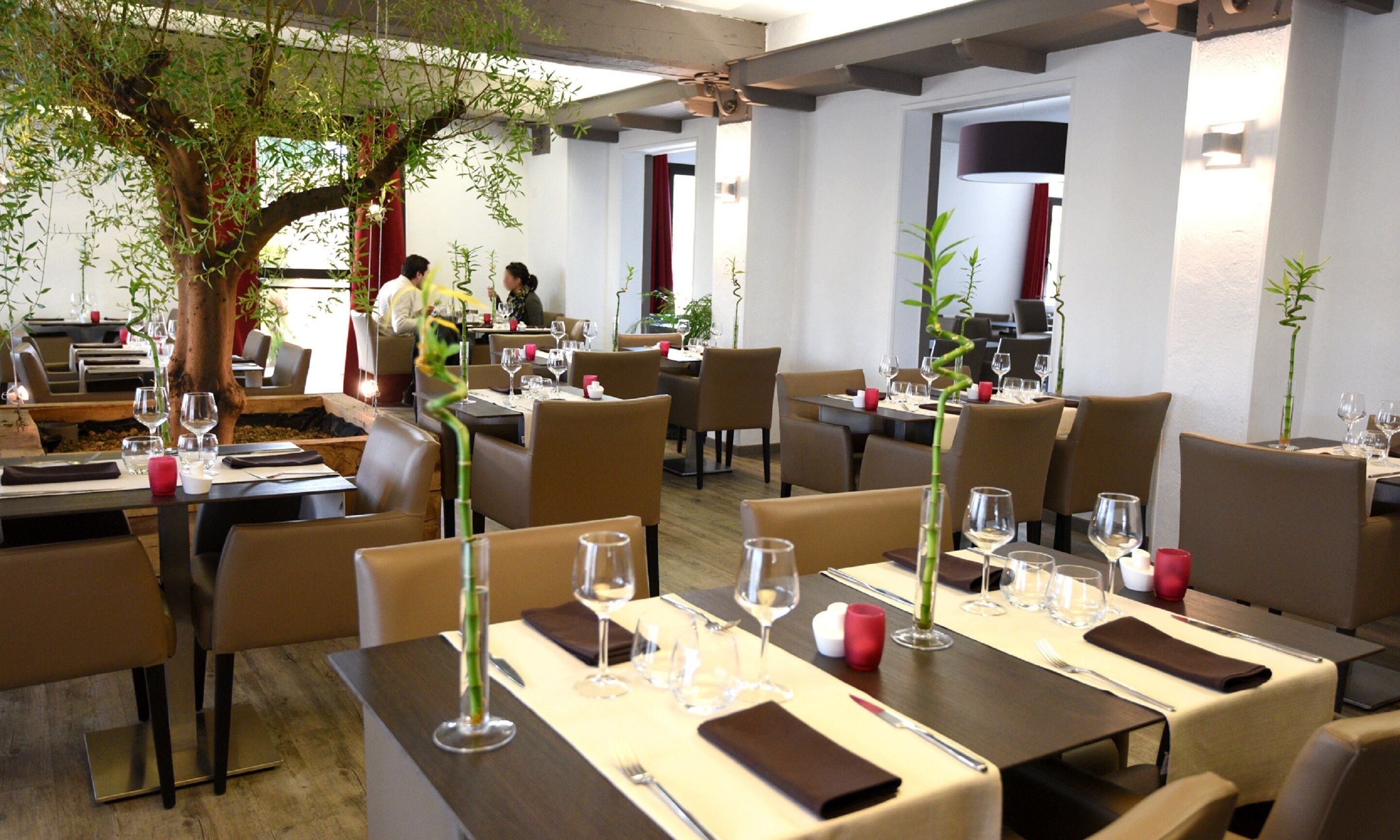 Een restaurant met gedekte tafels, stoelen en een grote boom in het midden.