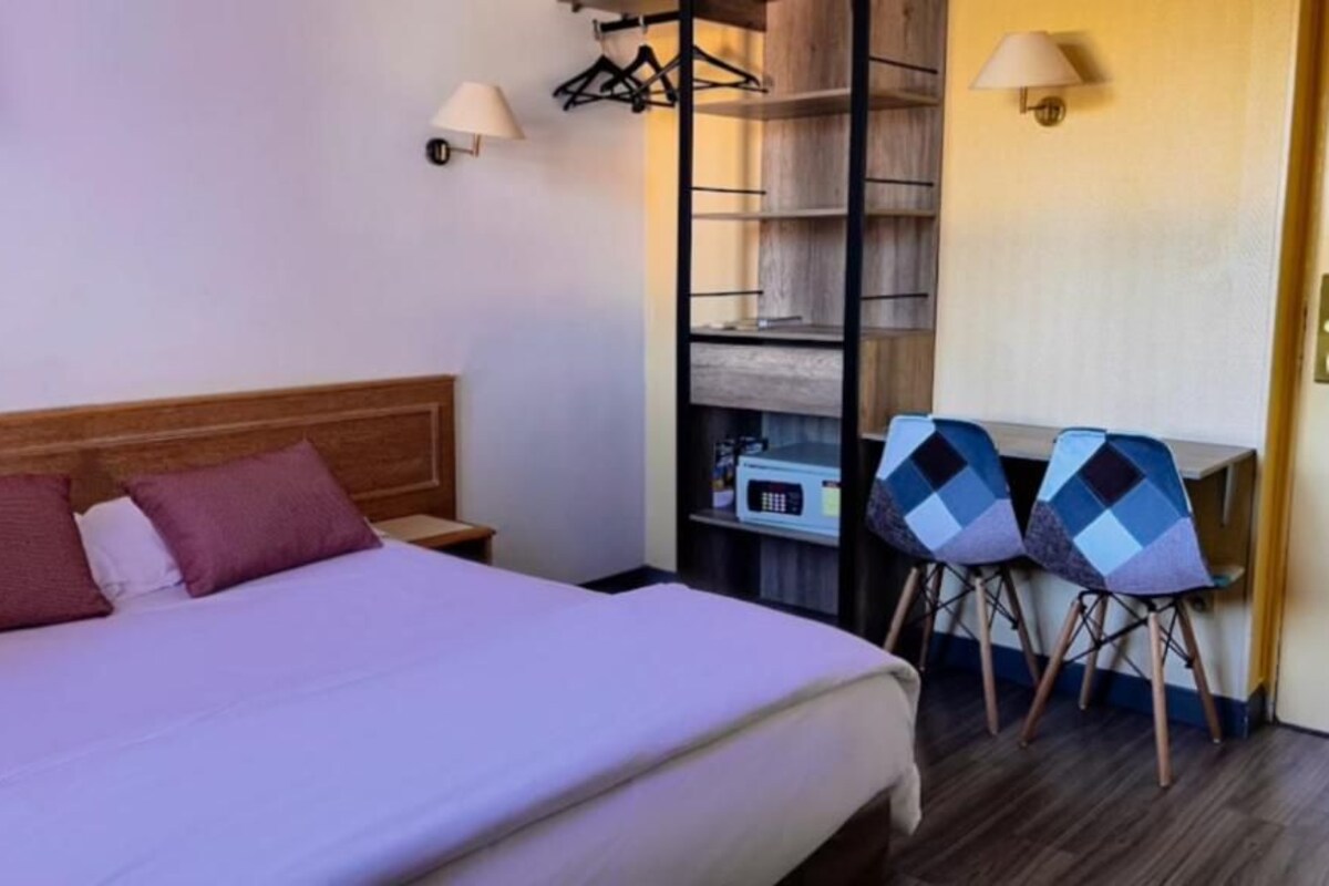 A hotel room with a bed, a desk with two chairs, and a wardrobe.