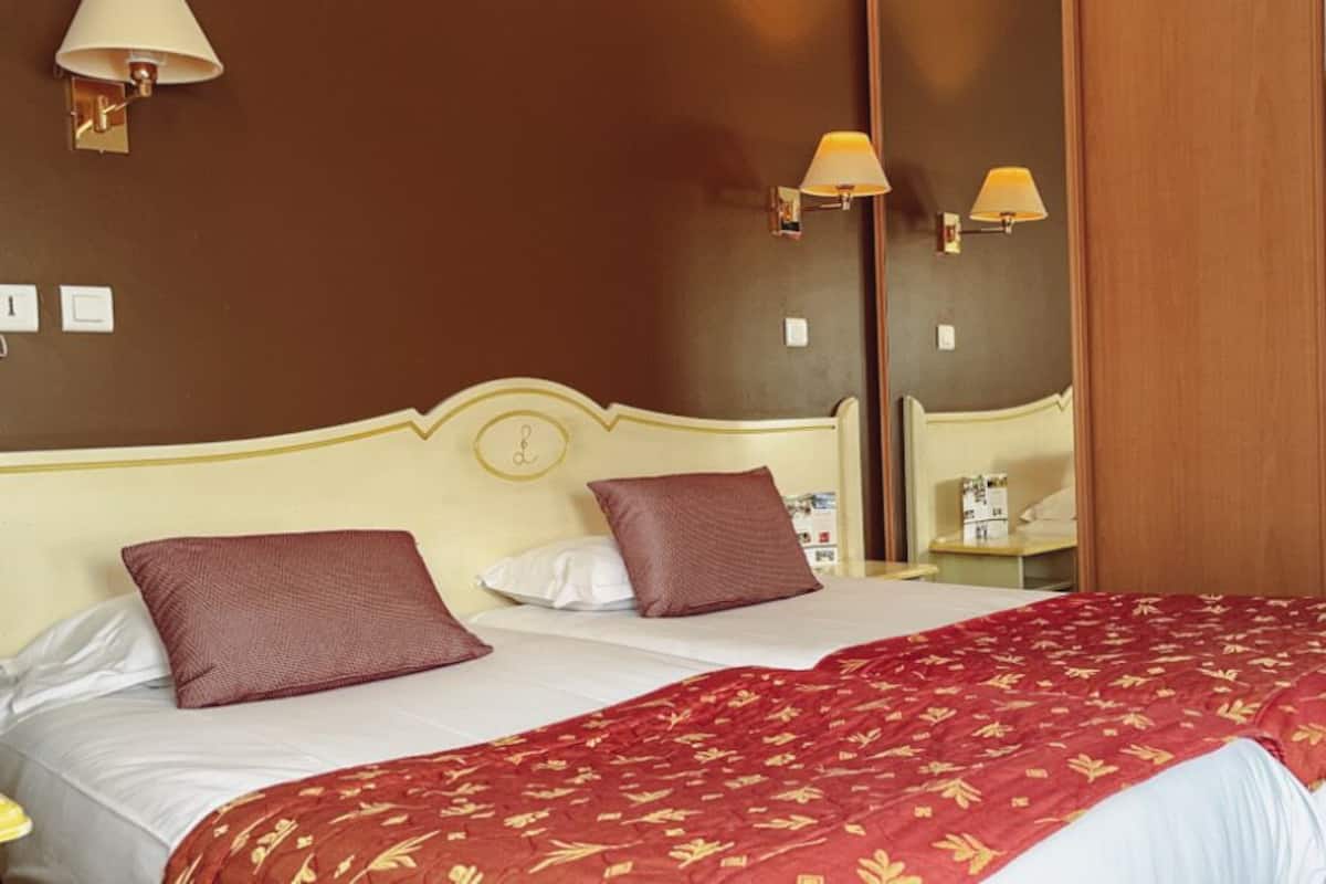 A hotel room with two beds, each with a red and white bedspread, and two wall-mounted lamps.