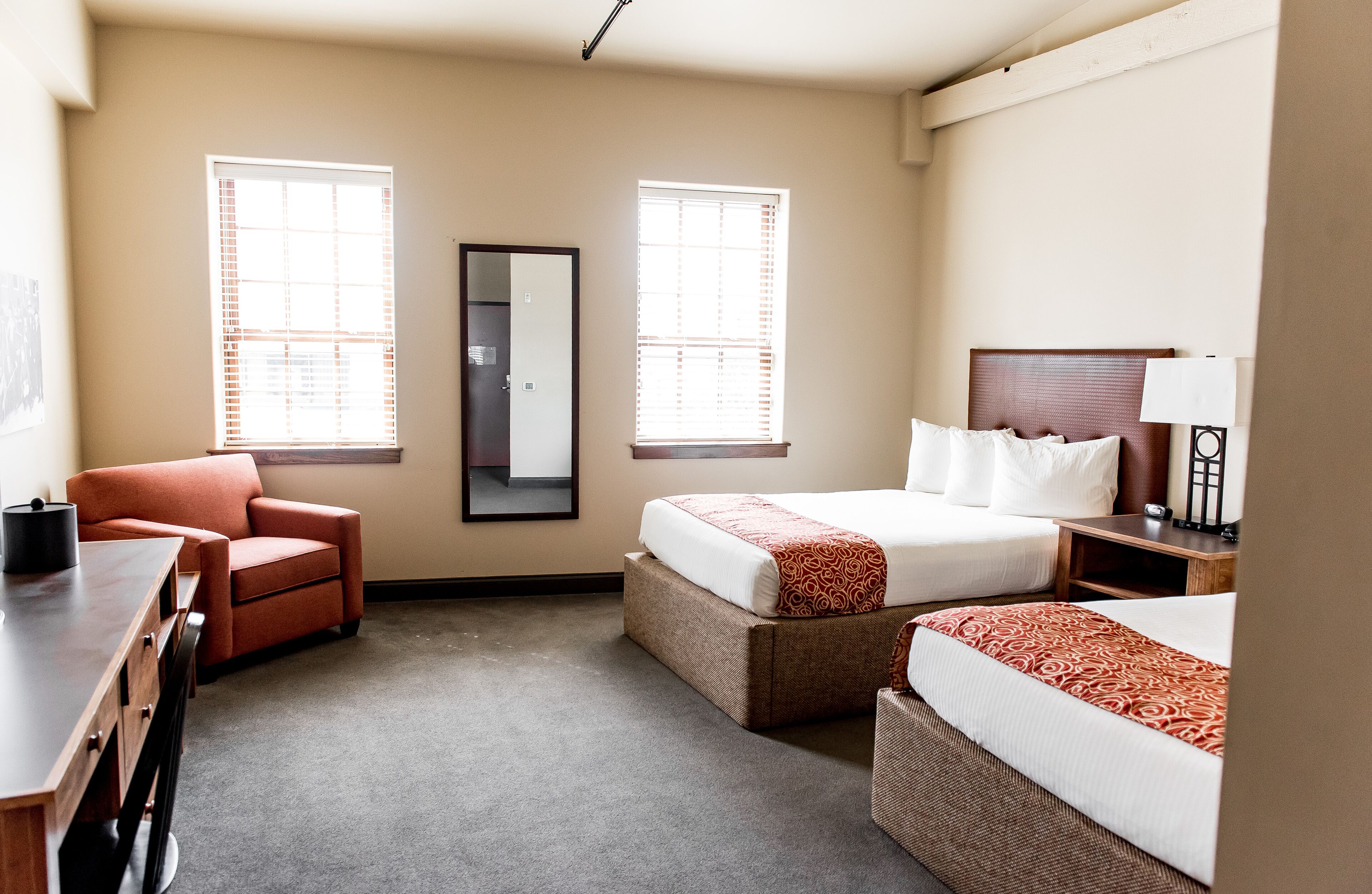 Quarto de hotel com duas camas, uma mesa, uma cadeira e duas janelas com persianas.