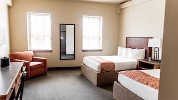 Habitació d'hotel amb dos llits, un escriptori, una cadira i dues finestres amb persianes.