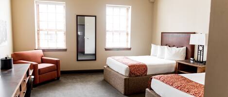Quarto de hotel com duas camas, uma mesa, uma cadeira e duas janelas com persianas.
