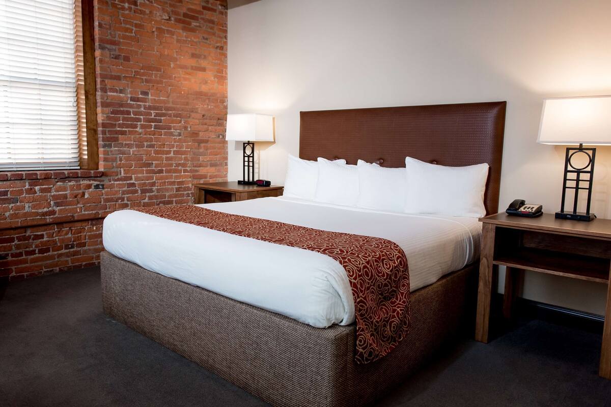 A hotel room with a large bed, a brick wall, and two bedside tables with lamps.