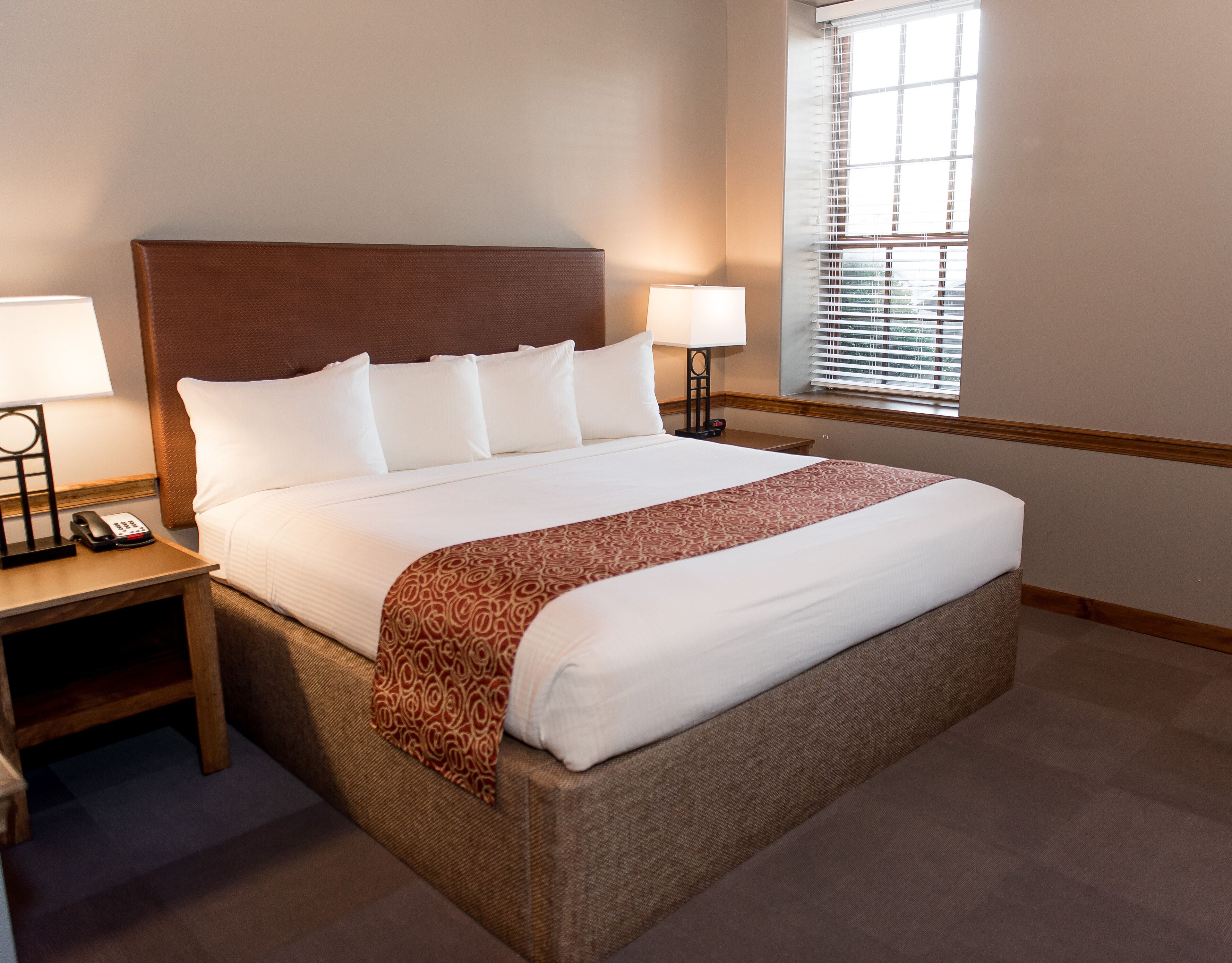 A hotel room with a large bed, two bedside tables, a telephone, and a window with blinds.