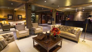A spacious lobby with a large, tufted sofa, several armchairs, a wooden coffee table, and a reception desk.