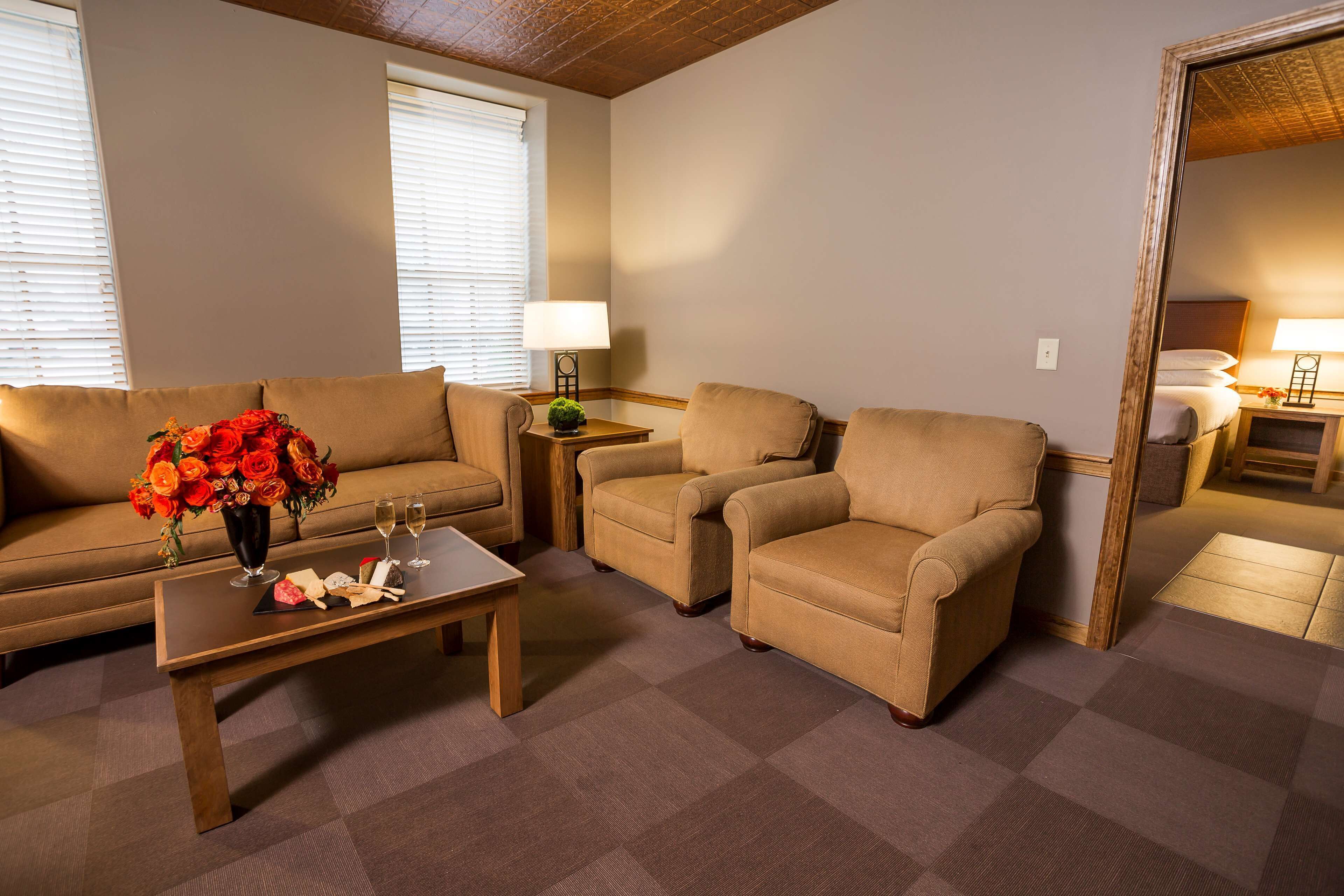 A room with a sofa, two armchairs, a coffee table with a vase of flowers, and a mirror.