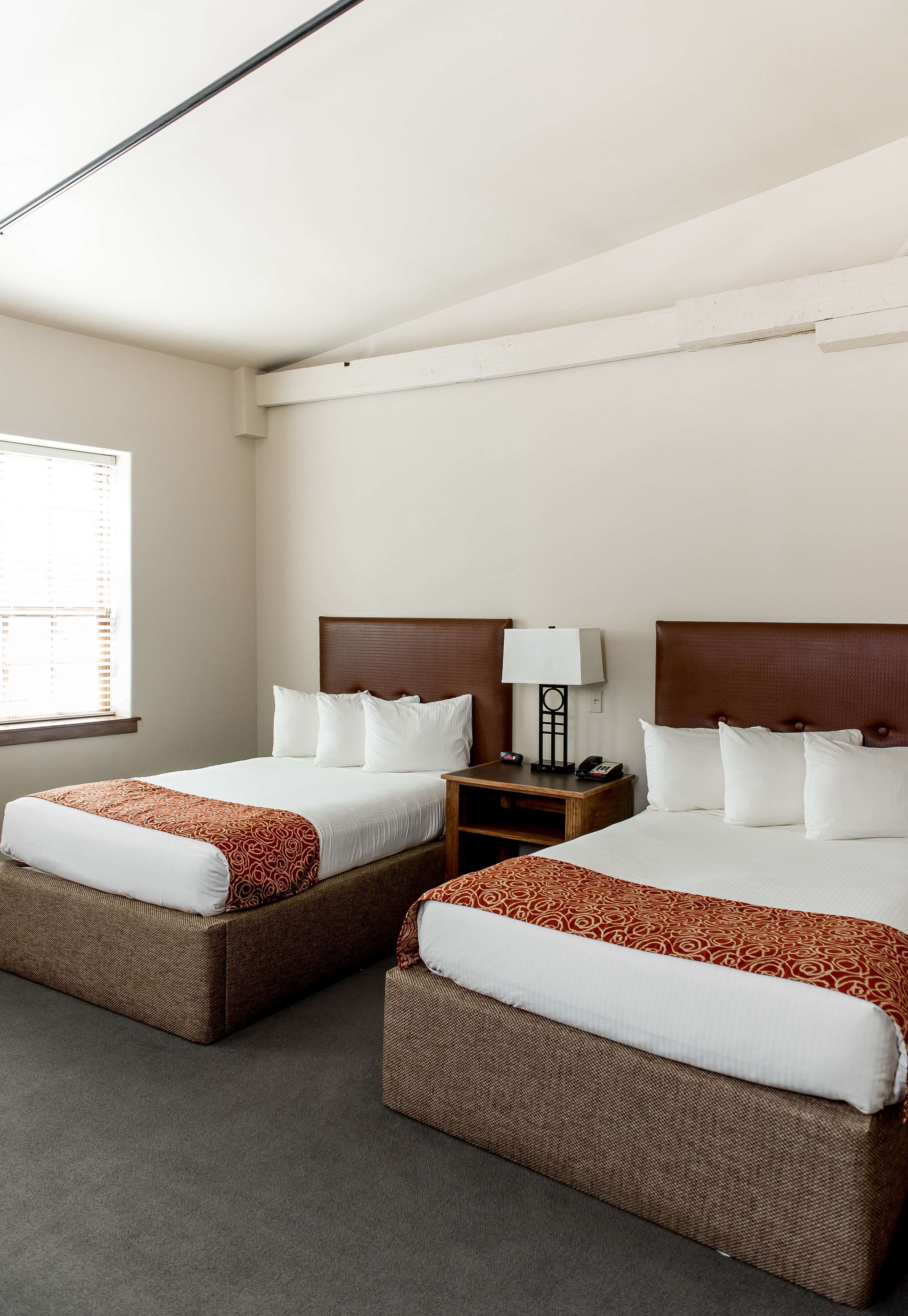 Een hotelkamer met twee bedden, een nachtkastje en een raam met jaloezieën.