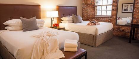 A hotel room with two beds, a bench, a nightstand with a lamp, and a large mirror.