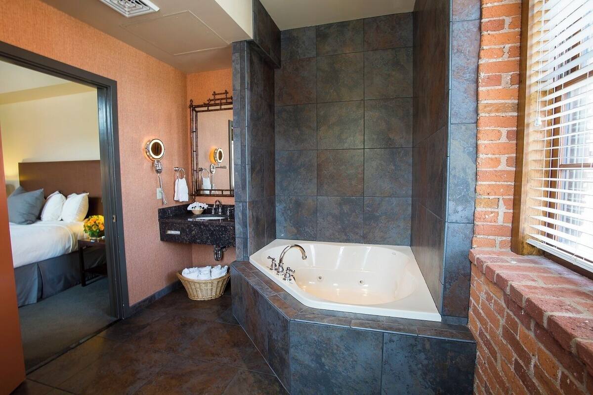 A modern bathroom with a large bathtub, a vanity with a mirror, and a wicker basket of towels.