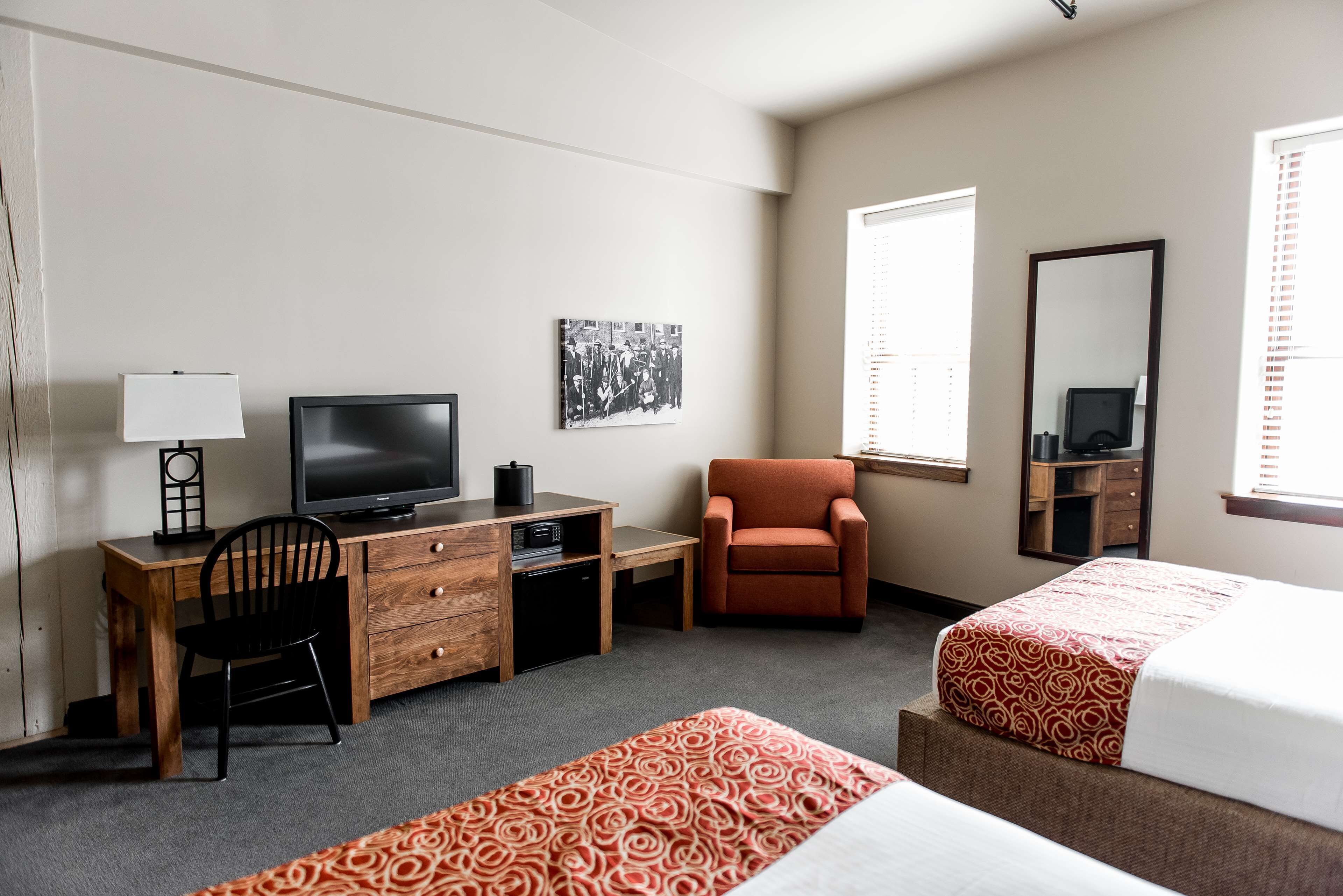 Ett hotellrum med en säng, ett skrivbord med en tv, en stol, en spegel och ett fönster.