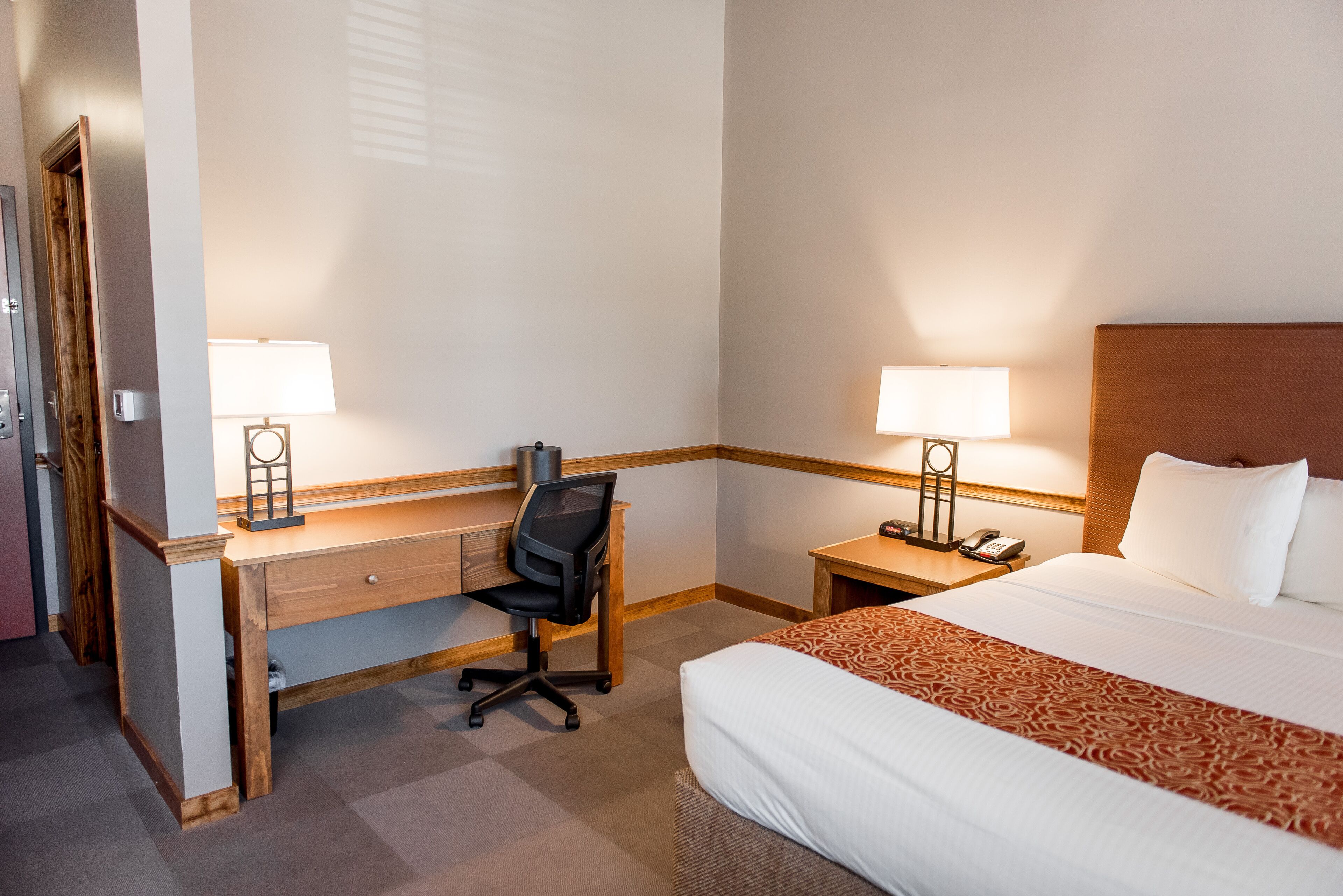Una habitación de hotel con cama, escritorio, dos lámparas y teléfono.