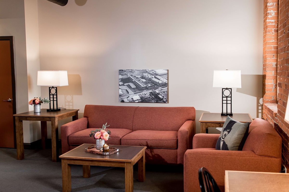 A cozy living room with a red sofa, two side tables with lamps, a coffee table with a vase of flowers, and a framed black and white photo on the wall.