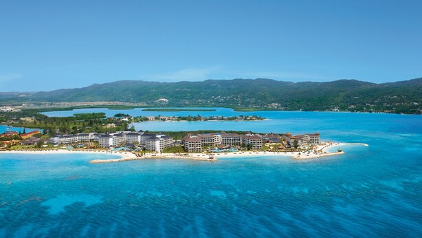 An aerial view of a resort with multiple buildings, a beach, and clear blue waters.