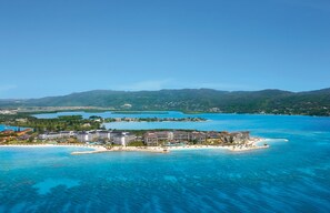 An aerial view of a resort with multiple buildings, a beach, and clear blue waters.