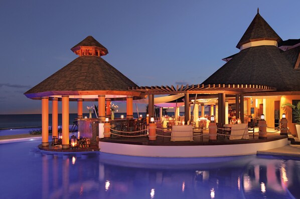 A resort with a pool, a bar, and a covered seating area with a view of the ocean.