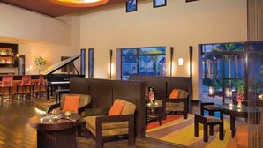 A spacious lobby with a grand piano, comfortable seating, and large windows offering views of the outdoors.