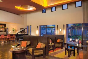 A spacious lobby with a grand piano, comfortable seating, and large windows offering views of the outdoors.
